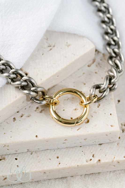 A chunky, silver chain link necklace with a gold spring gate front-closure clasp on it so you can add charms to it.