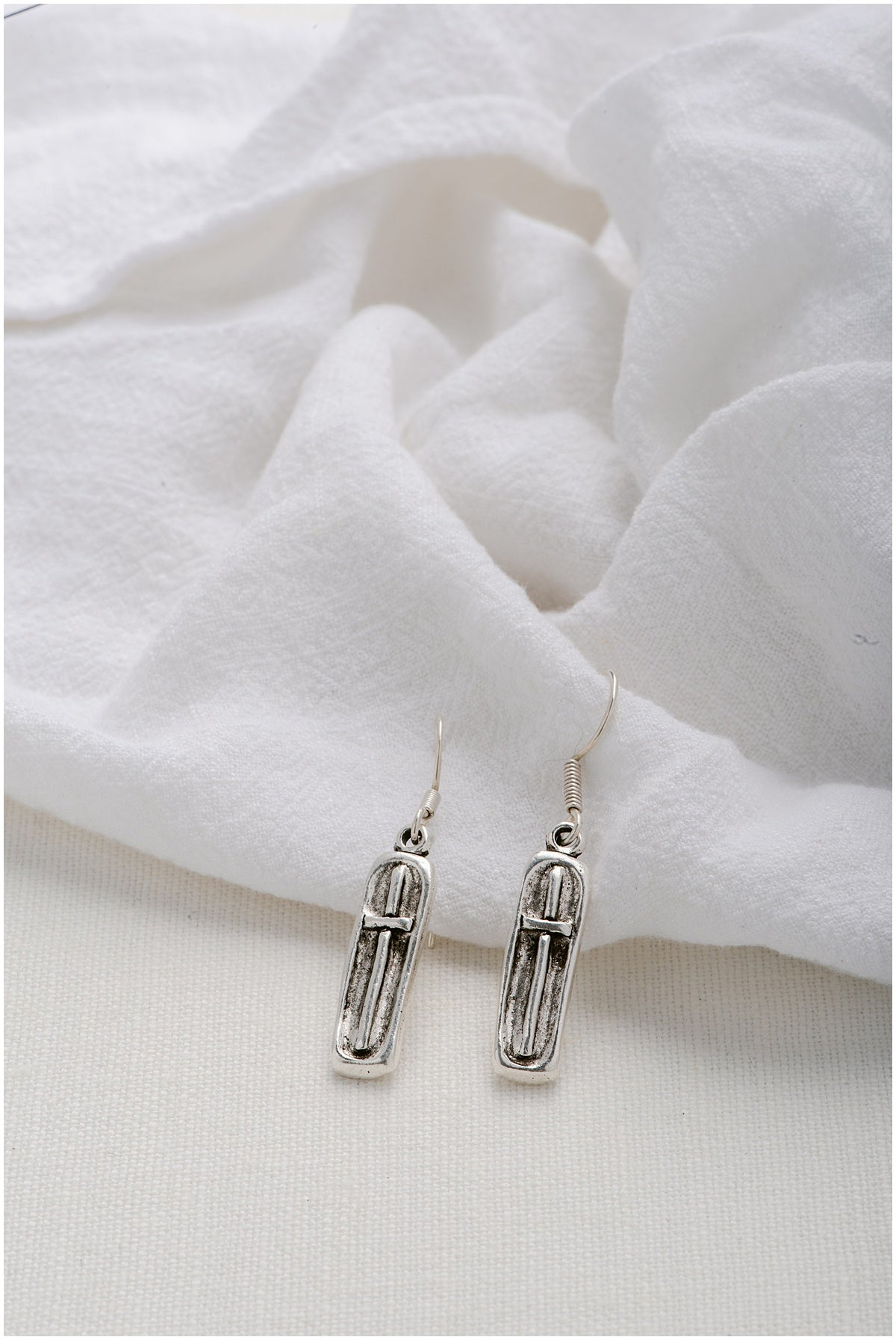 A pair of silver, rectangular earrings with a cross on top.