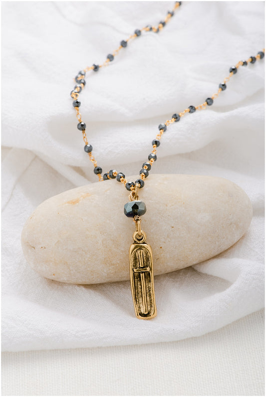 A gold beaded chain with a gold, rectangular pendant with a cross on it.