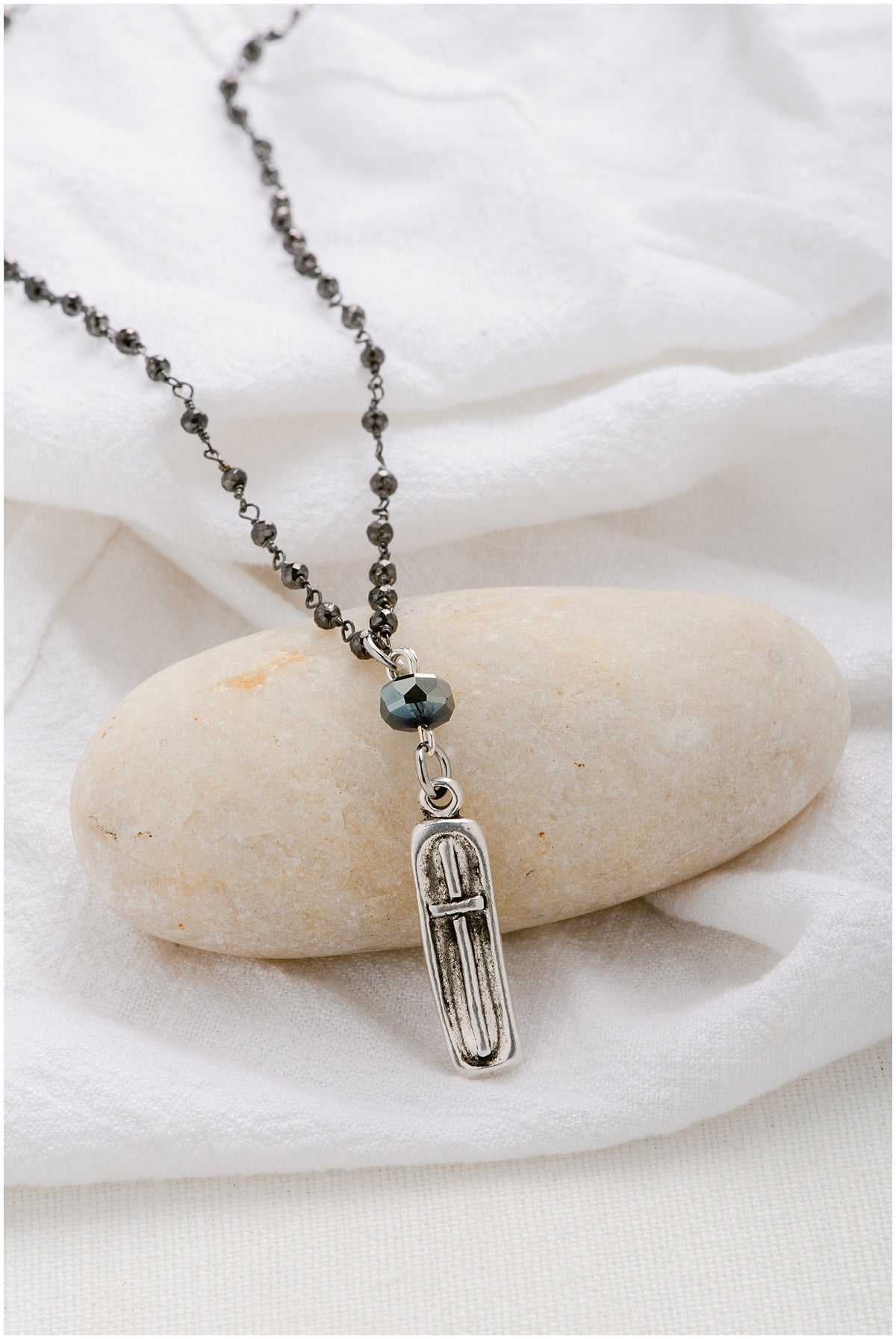 A silver beaded chain with a silver, rectangular pendant with a cross on it.