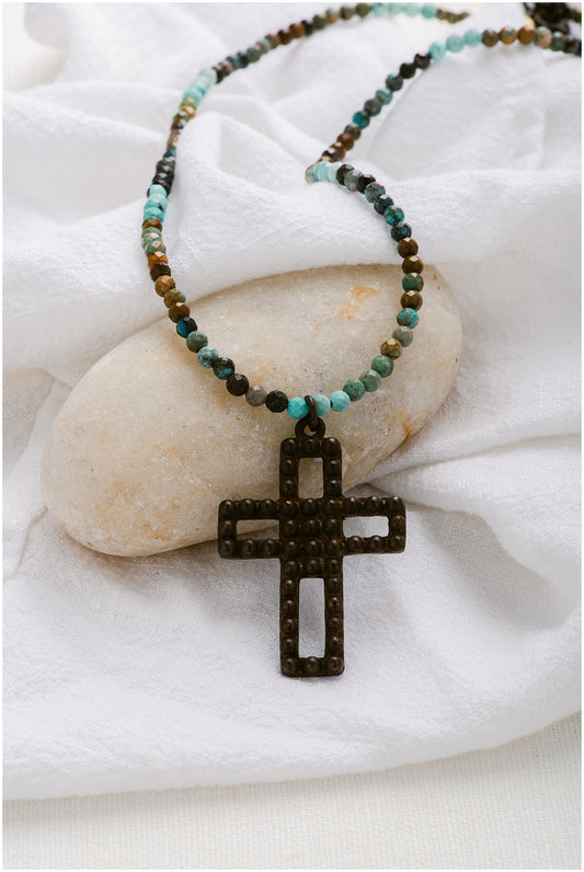 A cross necklace with turquoise and black beads.