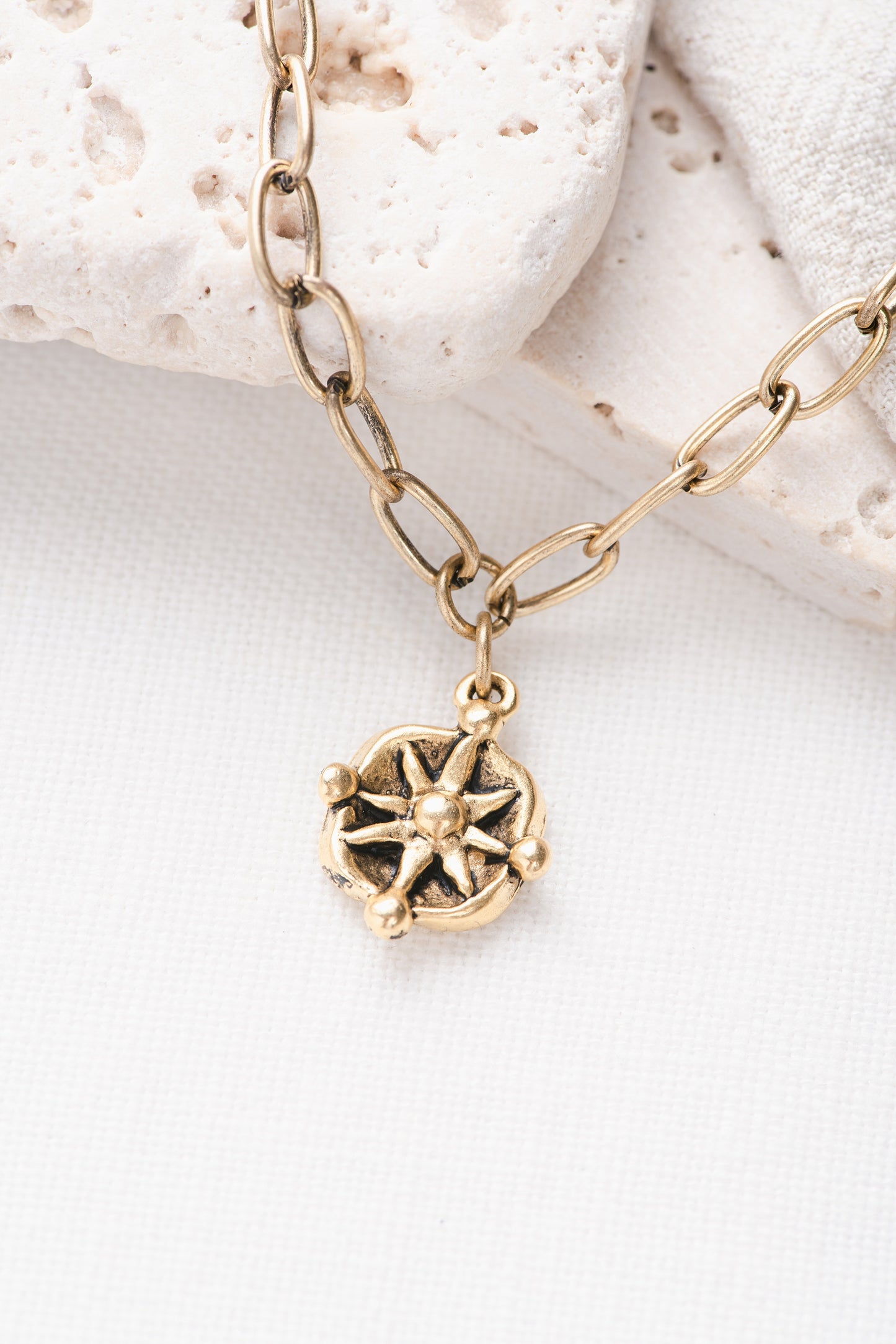 A gold paperclip chain necklace with a compass pendant on it.