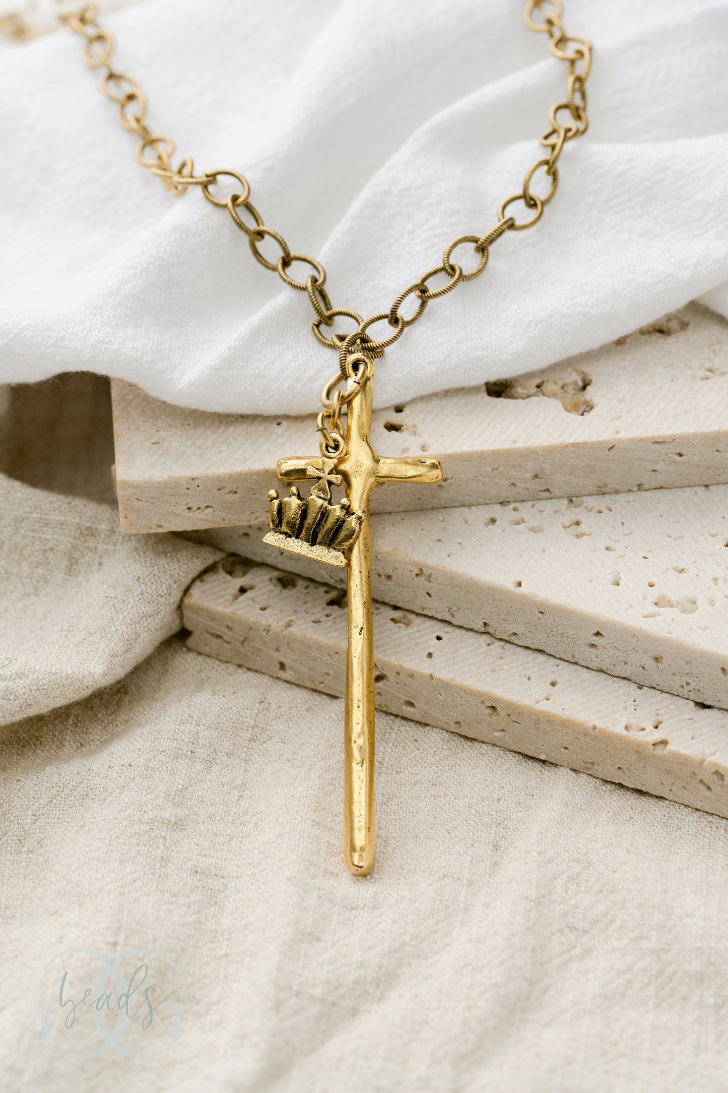 A gold necklace featuring a long, hammered cross with a crown on it.