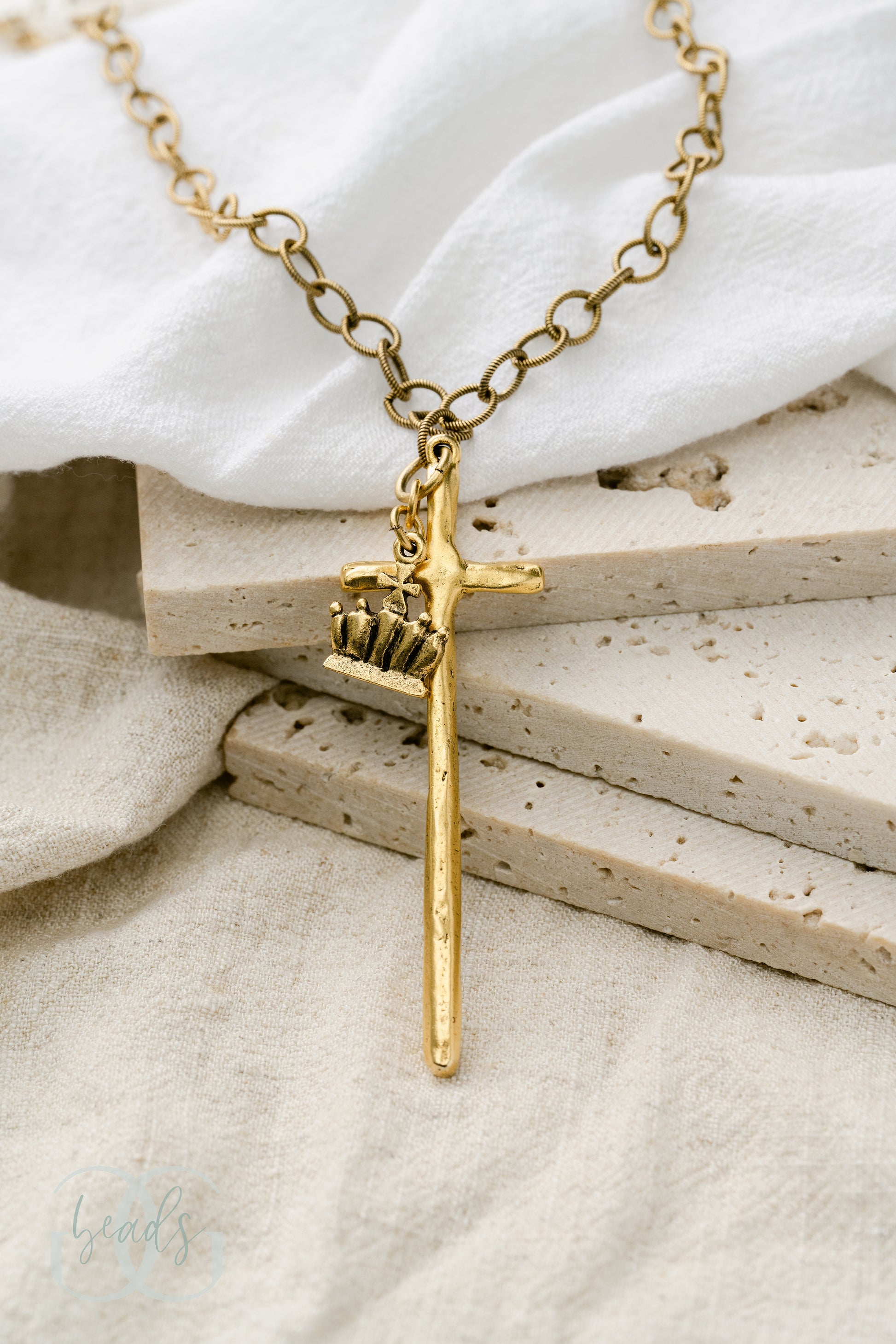 A gold necklace featuring a long, hammered cross with a crown on it.