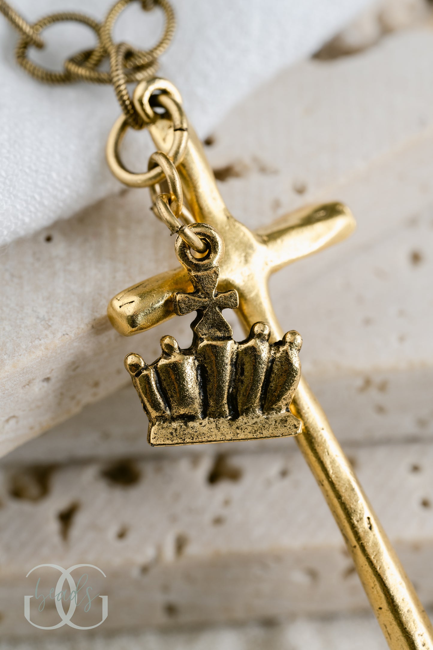 A gold necklace featuring a long, hammered cross with a crown on it.