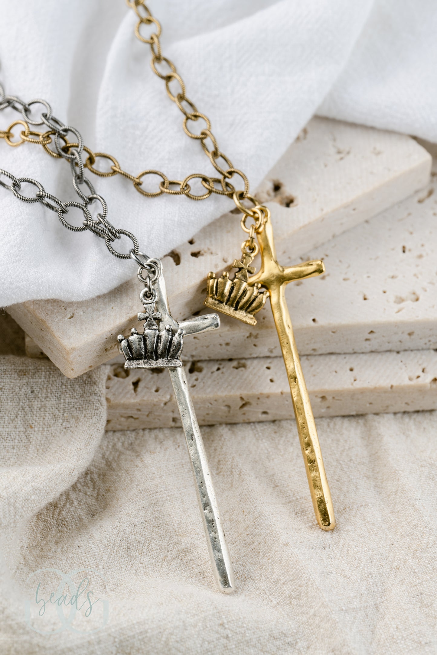 A necklace featuring a long, hammered cross with a crown on it. Shown here in silver and gold.