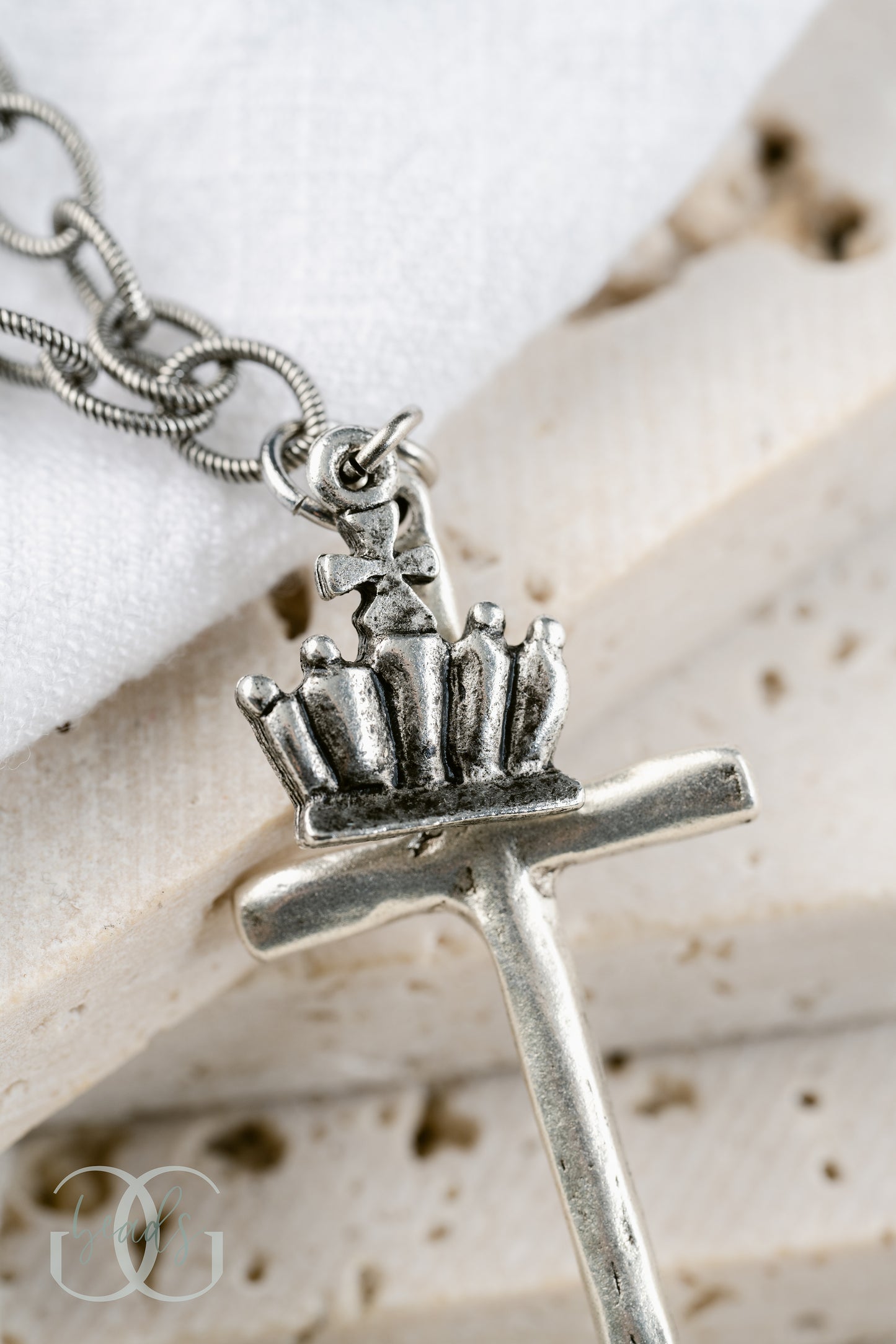 A silver necklace featuring a long, hammered cross with a crown on it.