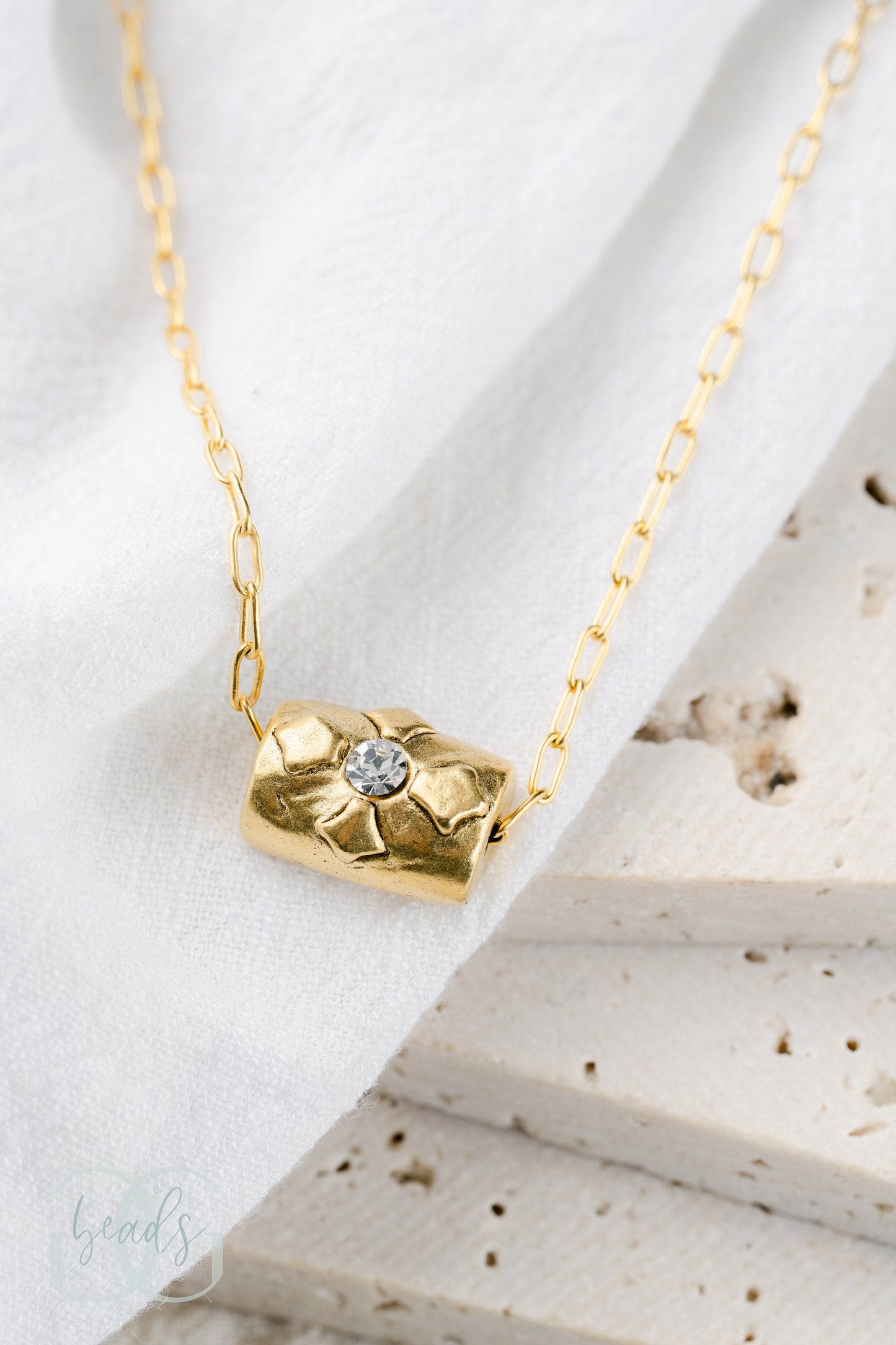 A delicate gold chain holds a white crystal and a floating cross bead, symbolizing grace and faith.
