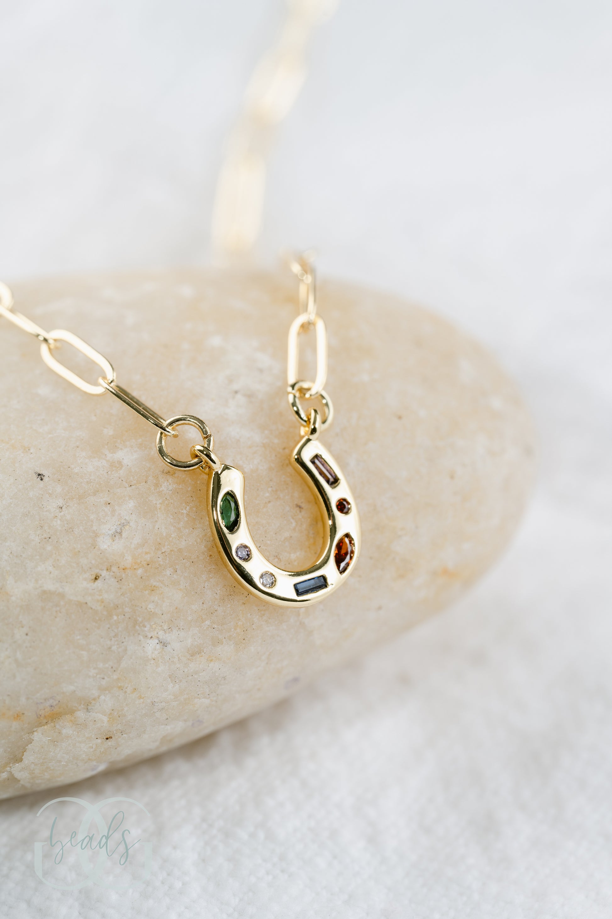 A gold horseshoe necklace on a dainty chain with seven crystals in it. The crystals are green, white, blue, and red.