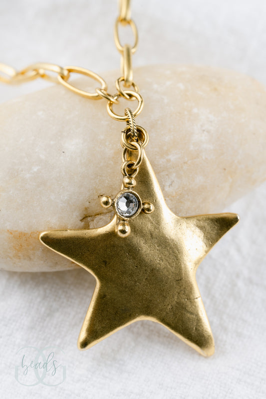 A gold chain featuring a large gold star pendant with a small crystal hanging from it.