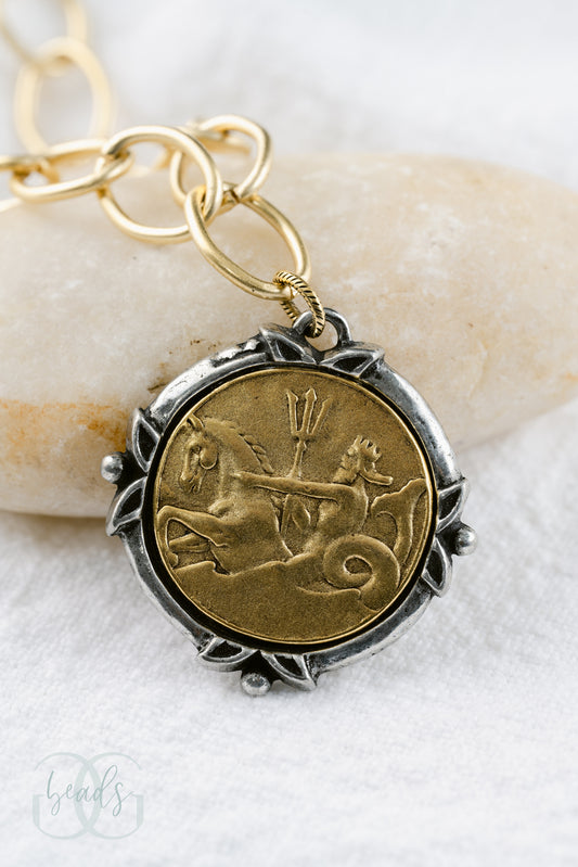 A chunky gold chain with a coin pendant. The outside of the coin is silver while the inside is gold featuring Poseidon riding a horse.