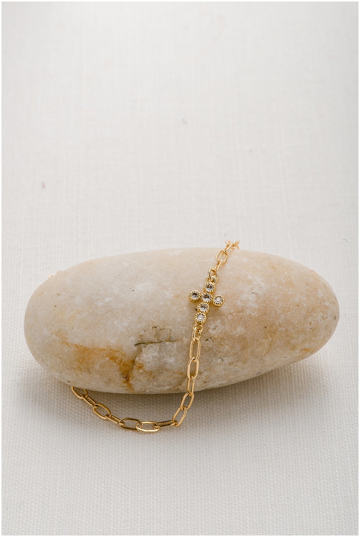 A gold paperclip chain with a round cut crystal cross charm embedded in it.