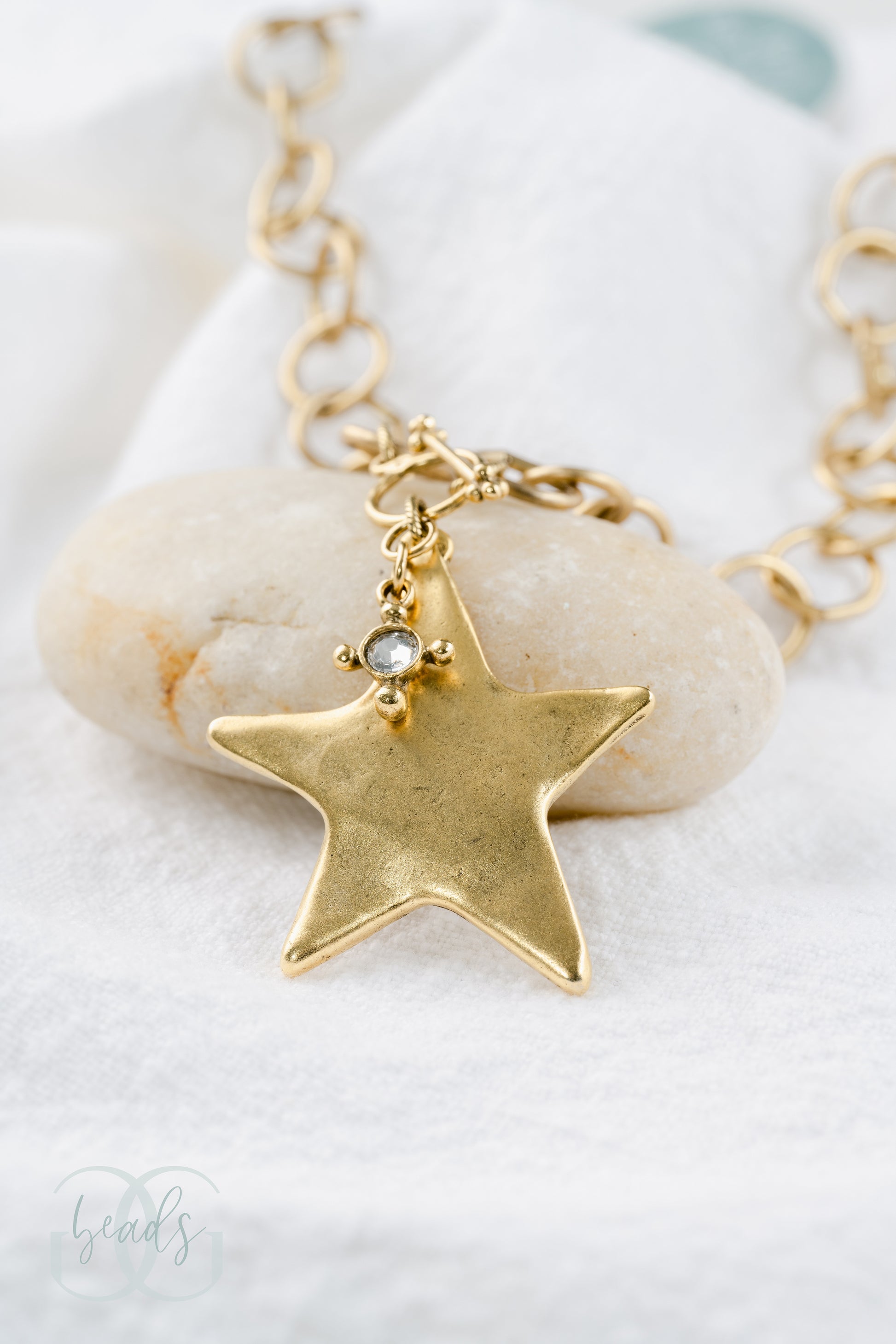 A chunky gold chain with a large star pendant with a crystal hanging from it.