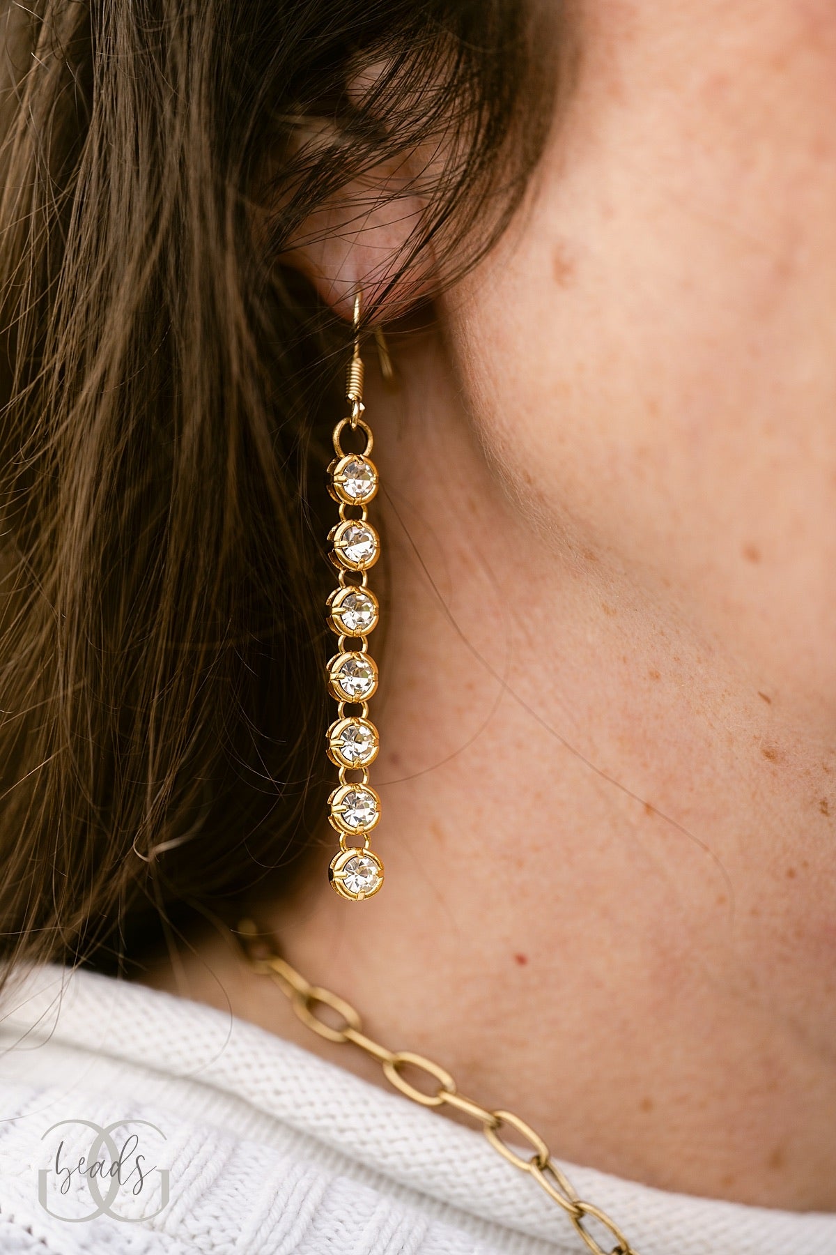 Our slim Leave a Little Sparkle Earrings - a pair of gold earrings with seven crystals dangling down from one another.