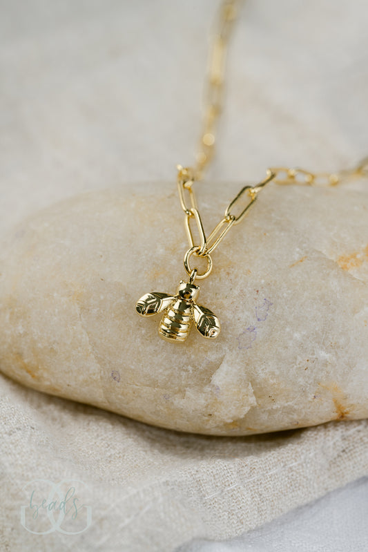 A gold chain necklace with a tiny, gold bee charm.