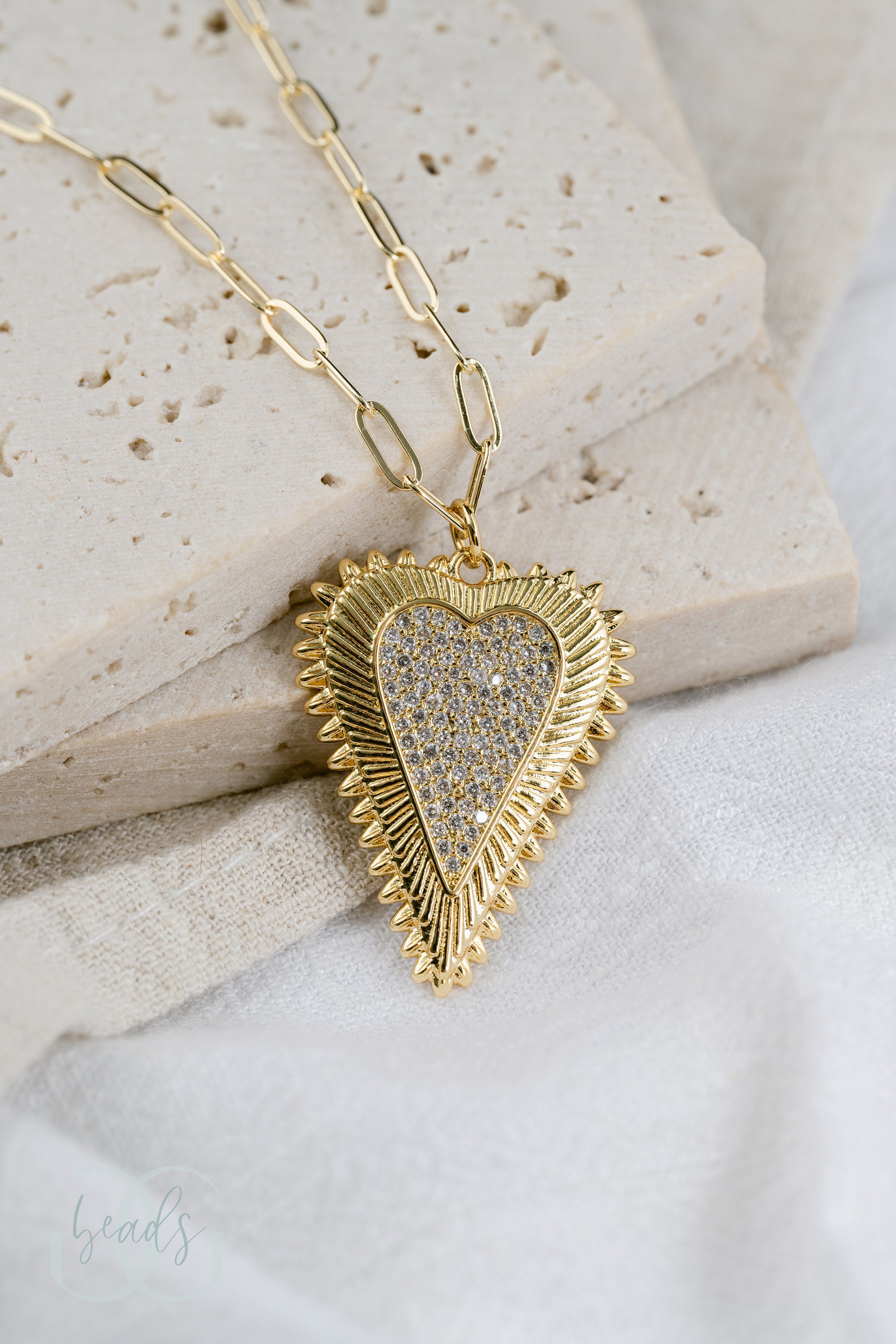 A gold paperclip chain necklace with a pave crystal heart pendant.