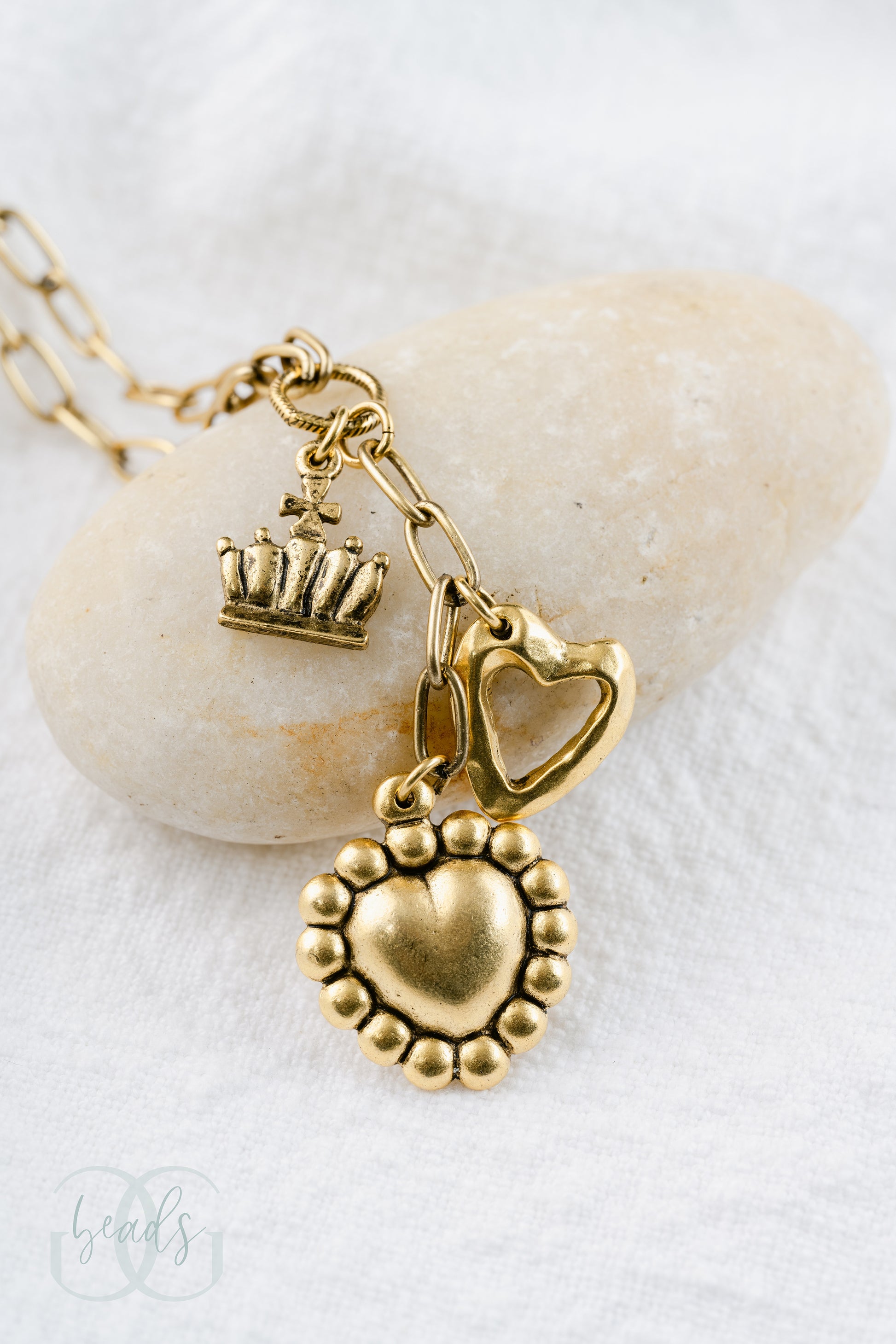 A gold lariat style necklace with an open heart charm, a crown charm and a puffy heart charm.