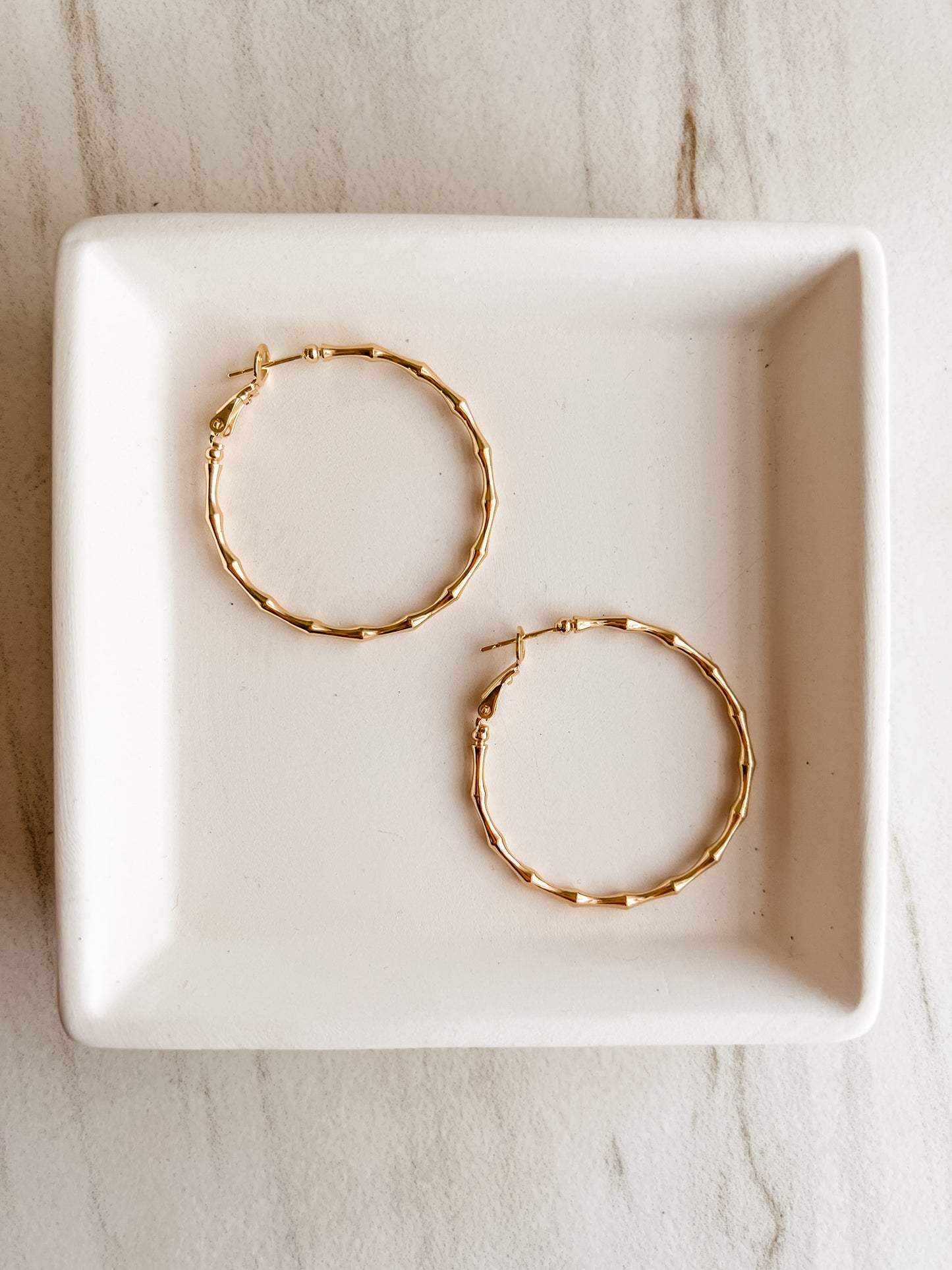 Gold hoop earrings designed with textured accents resembling bamboo stalks.
