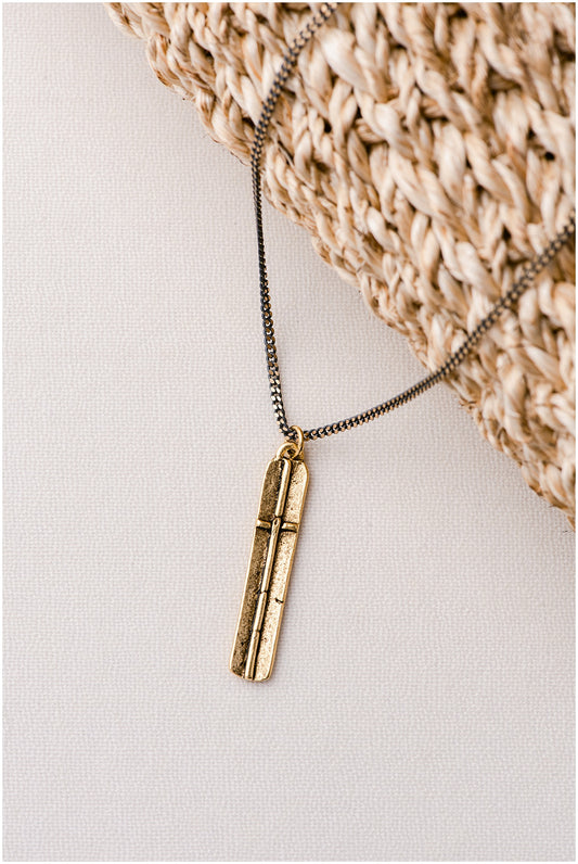 A rectangular, gold pendant with a cross on a light-colored pendant.