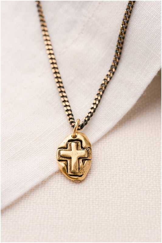 A gold pendant with a cross on it on a light-colored chain.