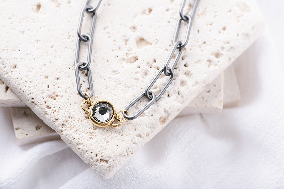 A gunmetal paperclip chain with a gold, crystal pendant.