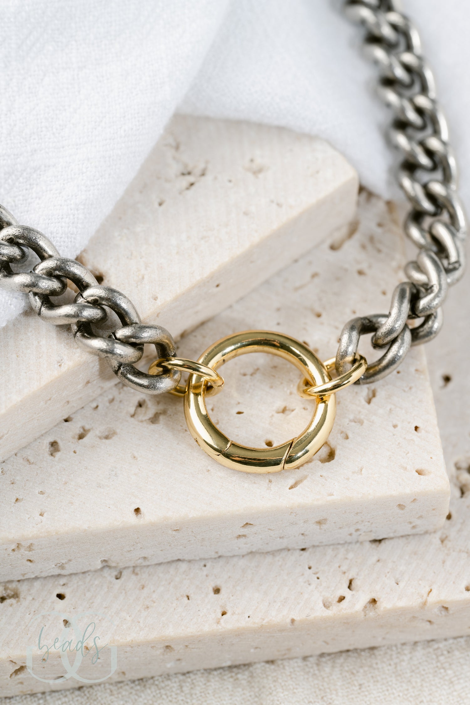 A chunky, silver chain link necklace with a gold spring gate front-closure clasp on it so you can add charms to it.