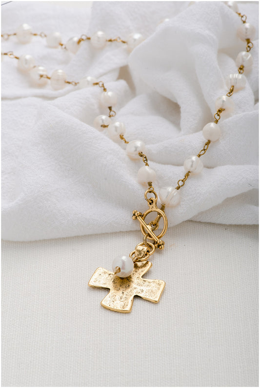 A gold chain lined with pearls with a gold, hammered cross pendant with a front-toggle closure. 