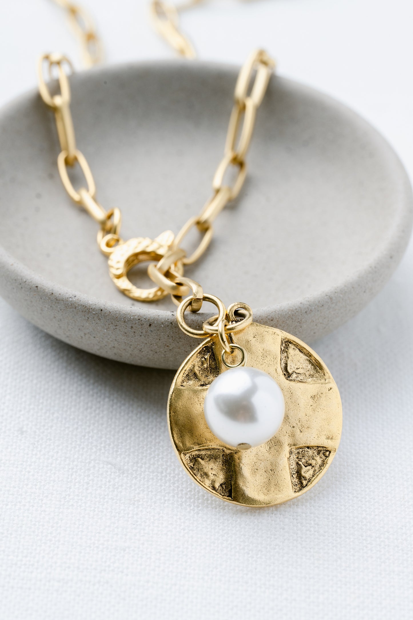 Gold necklace with a pearl pendant on a gray dish