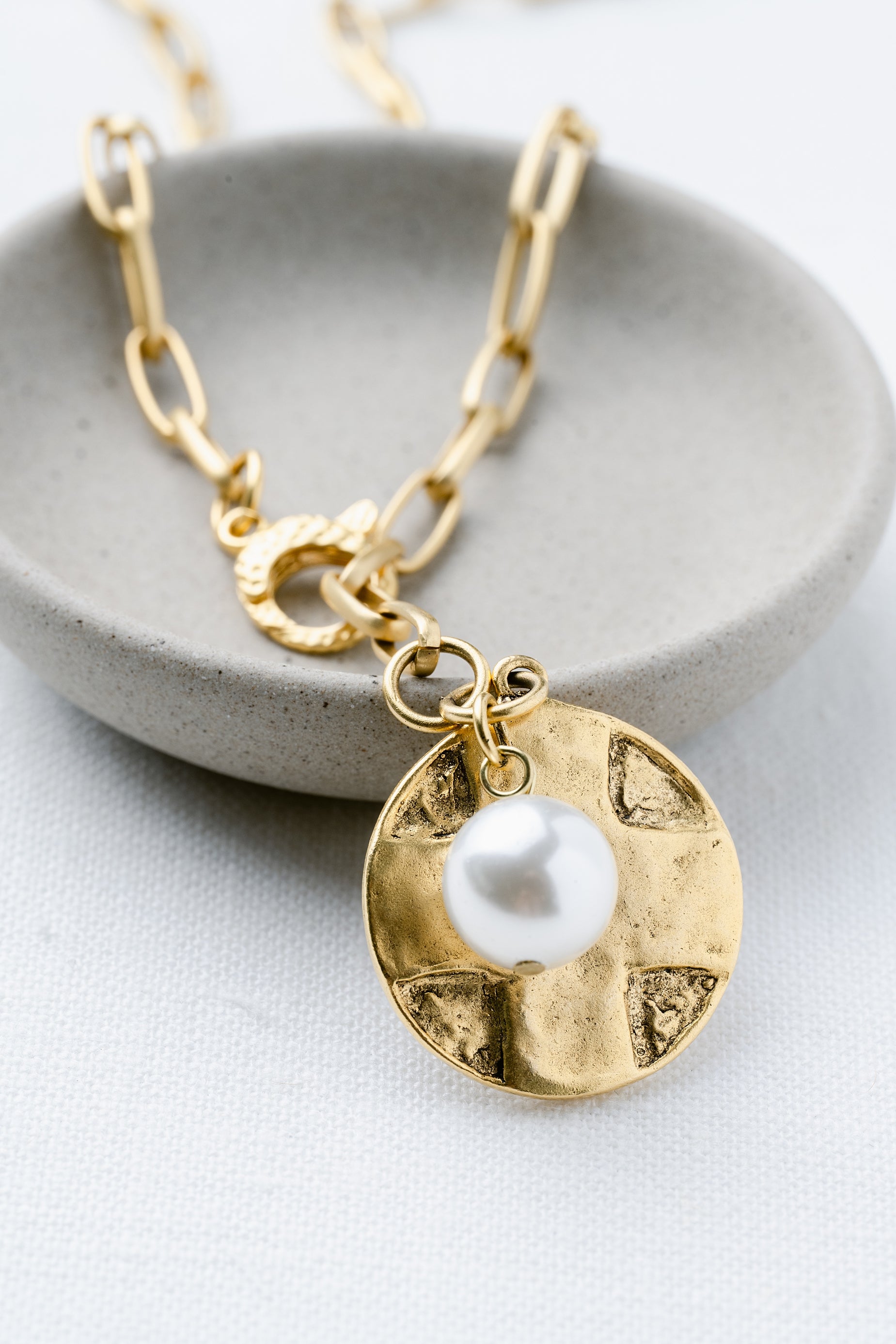 Gold necklace with a pearl pendant on a gray dish
