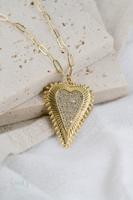 A gold paperclip chain necklace with a pave crystal heart pendant.
